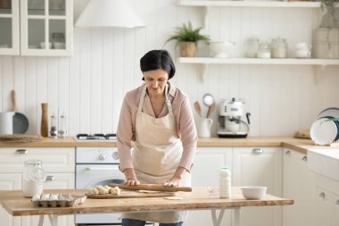 Emekli olgun bir kadın modern, rahat bir mutfakta tek başına önlük giyer, hamur işini ev yapımı pastaya hazırlar, evde pişirme sürecinin tadını çıkarır. Ev işleri, ev işleri, aile tarifi hazırlığı, aşçılık.