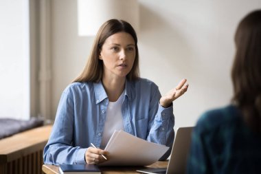 Ciddi şirket lideri, gayri resmi gömlekli bir kadın, iş başvurusunda bulunan bir kadınla görüşüyor, elinde kağıt belgeler, özgeçmiş, özgeçmiş tutuyor, karşımda oturan meslektaşımla konuşuyor.