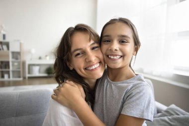 Neşeli güzel bir anne ve mutlu bir ergen kızın sevgiyle kucaklaşması, yüzlerine dokunması, kameraya bakması, gülümsemesi, beyaz dişlerini göstermesi, ev portresi için poz vermesi, video aramasında konuşması.