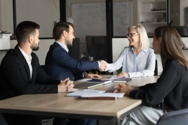Mutlu yaşlı iş kadını takım toplantısında genç proje yöneticisine tokalaşıyor. İş arkadaşları işbirliği, ortaklık, tokalaşma, takım çalışması, anlaşma