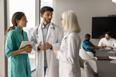 Beyaz üniformalı bir grup pratisyen doktor tıp mesleğini tartışıyor, sağlık konferansında doktorluk yapıyor, toplantı odasında birlikte duruyor, sohbet ediyorlar.