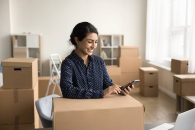 Pozitif Hintli web mağazası yöneticisi kız taşımacılık için karton kutu paketliyor, müşteriye ürün gönderiyor, cep telefonunda lojistik uygulama kullanıyor, sipariş veriyor, nakliye hizmeti veriyor.