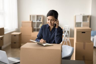 Şirin Hintli genç bir depo müdürü internetten müşteriye alışveriş yapıyor, cep telefonuyla paketlenmiş karton kutuda konuşuyor, notlar yazıyor, işlem sırasını hazırlıyor.