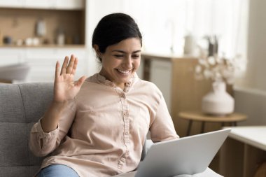 Mutlu Hintli serbest çalışan kadın monitöre el sallıyor, selamlaşarak selam veriyor, video görüşmesiyle konuşuyor, gülümsüyor, dizüstü bilgisayarını internet iletişimi için kullanıyor.