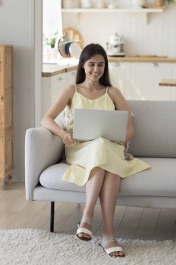 Mutlu, genç, güzel, yetişkin bir kız Webinar izliyor, film izliyor, evde eğleniyor, internet iletişimi kuruyor, dinleniyor, kanepede oturuyor, internette konuşuyor, gülümsüyor, gülüyor.,