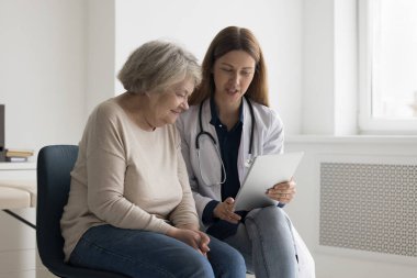 Yaşlı bir kadına tıbbi muayene sonucu veren yaşlı ve nişanlı bir doktor. Danışmanlık için tıbbi uygulamayı kullanıyor, hastaya elektronik reçete gönderiyor.