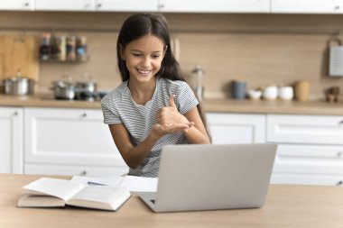 İşitme engelli, evde dizüstü bilgisayar kullanan, online çalışan, video konferansında konuşan, sağır dili kullanan, ekranda el işaretleri gösteren pozitif bir anaokulu öğrencisi.