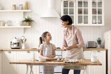 Yaşlı ve tatlı küçük kız konuşuyor, ev mutfağında birlikte yemek pişiriyor, önlük giyiyor, aile tatilinde ev yapımı hamur işleri hazırlıyor. Tecrübe, beceri, hobi ve çocuk gelişimi