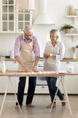Son sınıf emekli çift ev yemekleri yapıyor, önlük giyiyorlar, kahvaltıda çörek pişiriyorlar, ev mutfağında tatlı hazırlıklarının keyfini çıkarıyorlar, konuşuyorlar, masada hamurlar yuvarlıyorlar. Dikey çekim