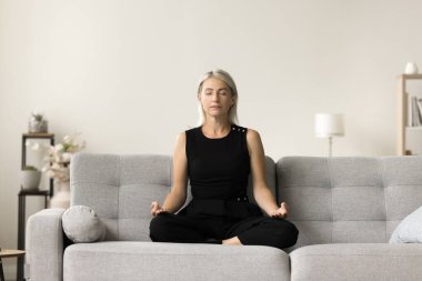 Nilüfer çiçekli kanepede oturan, Zen jestini saklayan, rahatlama, farkındalık, sakinleşme, stres atma teknikleri geliştirmek için gözleri kapalı meditasyon yapan olgun yogi bayan.