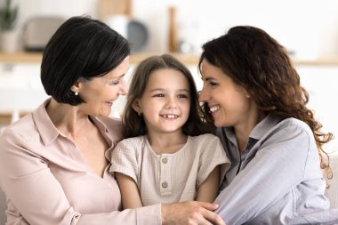 Çoklu nesil kadın ailesinin uyum ilişkileri. Yaşlı büyükanne, küçük torun ve küçük yetişkin kızla vakit geçirmenin tadını çıkar. Kanepede birlikte otur, sarıl, sıcak bir iletişim kur, kapat.