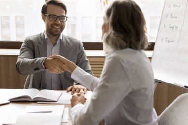 Başarılı genç iş adamı olgun iş ortağı kadınla anlaşmaya varıyor, beklenen anlaşma, iş, toplantıda iş kadınıyla el sıkışmak, gülümsemek, gülmek.