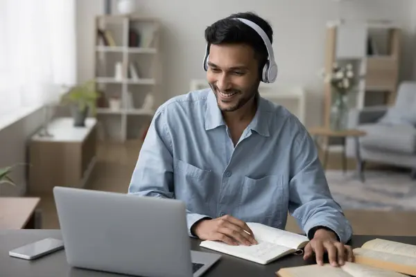 stock image Cheerful young adult Indian student guy in headphones watching learning video on laptop, talking on video call to teacher, studying online, using Internet technology for education