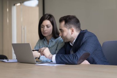 İki ciddi milenyum çalışanı proje üzerinde birlikte çalışıyor, ofisteki dizüstü bilgisayarın başında çalışıyor, ekranı gösteriyor, gösteriyor, konuşuyor, yazılım ürünlerini tartışıyor.