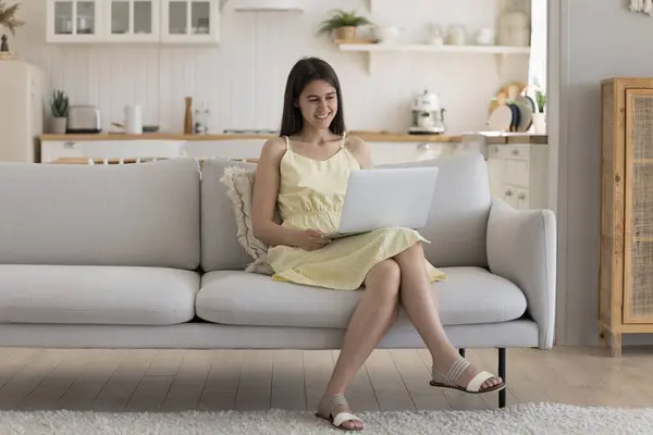 stock image Cheerful happy late teenage gen Z student girl using online application on laptop, talking on video call, watching webinar, movie, enjoying leisure, resting on home sofa with gadget