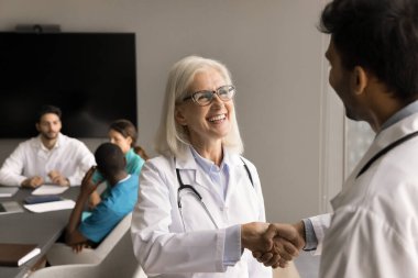 Neşeli kıdemli doktor kadın genç erkek meslektaşıyla tokalaşıyor, patron, şef, gülüyor, iyi iş sonuçlarından memnun. Tıp çalışanları el sıkışıyor, toplantıdan zevk alıyor, işbirliği yapıyor.