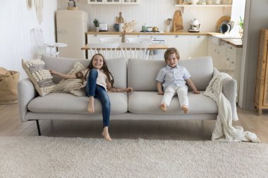 İki mutlu erkek kardeş ve kız kardeş evdeki yumuşak rahat kanepede dinleniyor, kameraya bakıyor, gülüyor, boş zamanların tadını çıkarıyor, çocukluğunu rahat, modern bir evde geçiriyor. Tam boy portre