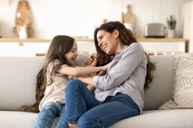 Güzel İspanyol annenin küçük tatlı kızını gıdıklaması kanepeye oturması, hafta sonları oynaması, eğlenmesi, boş zamanların ve aktif oyunların tadını çıkarması, aşkı hissetmesi, bağlılığını göstermesi. Aile bağları, evde oyun zamanı, annelik.