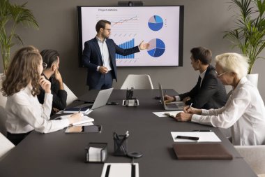 Güvenilir genç iş adamı pazarlama istatistik raporunu ortaklara, yatırımcılara sunuyor, toplantı, müzakere ve elektronik ekranda grafikler göstererek başlangıç projesini satıyor.