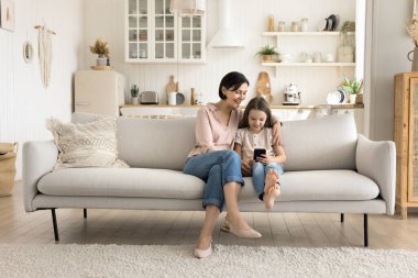 Büyük anne ve küçük torunu akıllı telefon kullanıyor. Çok nesilli aile internette vakit geçirir, oyun oynar, kanepeye oturup yeni uygulamaların tadını çıkarır. Eğlence, eğlence ve bilgi edinmek için modern teknoloji kullanımı