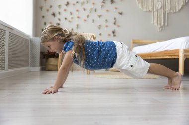 Evde egzersiz yapan tatlı bir çocuk, el ve ayak desteğiyle yerde ön kalas yapıyor, yoga yapıyor, jimnastik dersi alıyor, spor aktivitelerinden hoşlanıyor, çocukluk, aktif yaşam tarzı.