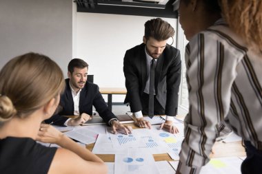 Odaklanmış iş ekibi birlikte satışları analiz ediyor, finansal istatistik raporlarını inceliyor, toplantı masasında dökümanları, şemaları tartışıyor, ekonomik grafikler hakkında konuşuyor.