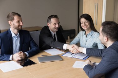 Pozitif orta yaşlı iş ortakları toplantı masası üzerinde tokalaşıyor, anlaşmayı kapatıyorlar, anlaşma üzerinde pazarlık ediyorlar, başarılı ortaklığı tartışıyorlar, takım çalışması, sözleşme, gülümseme.