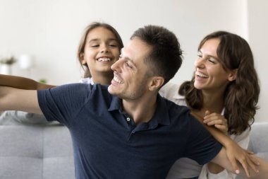 Mutlu ebeveynler, uçakla uçma oyunu oynayan, rahat koltukta oturan, gülen, gülen, eğlenen, ebeveynlikten keyif alan, ailece vakit geçiren, neşeli küçük kızlarını sırtlarına alıyor.