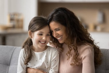 Olumlu güzel anne ve sevimli kız çocuğu konuşuyor, gülüyor, aile ilişkisinden zevk alıyor, sohbet ediyor, eğleniyor. Anne şefkati, çocuk kucaklaması, kanepe sevgisi, annelik keyfi.