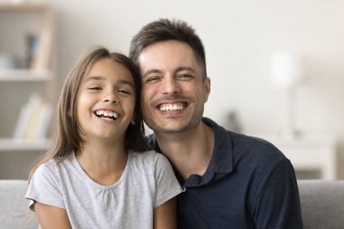 Neşeli yakışıklı baba ve kaygısız tatlı kız çocuğu dişlek gülüşlü kameraya bakıyor, aile diş bakımını destekliyor, sağlıklı beyaz dişler. Mutlu baba ve güzel kız evde portre resmi