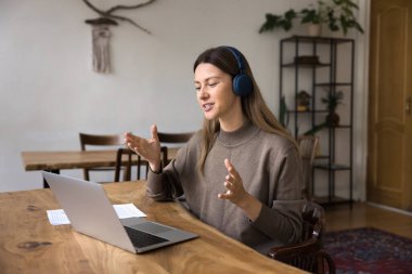 Kablosuz kulaklıklı olumlu proje yöneticisi kadın evden yaptığı video konferans görüşmesiyle konuşuyor, iş iletişimi için laptop kullanıyor, internet üzerinden yayın yapıyor, internet üzerinden yayın yapıyor.