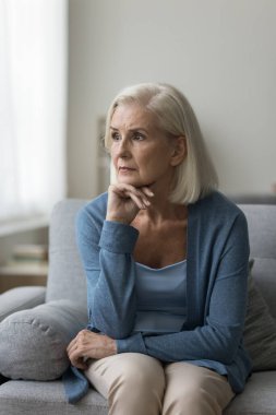 Düşünceli son sınıf öğrencisi kadın evde vakit geçirir, kanepeye oturur, uzaktan bakar, kaygı duyar, psikolojik sorun yaşar, geçmişi hatırlar, sağlık için endişelenir. Melankoli, nostalji, yalnızlık