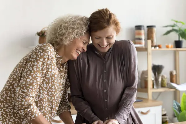 stock image Positive senior mom and adult daughter cooking dinner in home kitchen together, standing at table, having fun, laughing out loud, enjoying culinary hobby, family leisure