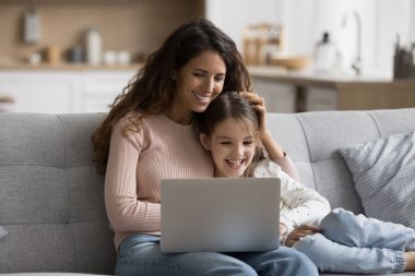 Mutlu anne ve küçük kız çocuğu dizüstü bilgisayarla eğleniyor, internetten film izliyor, online video görüşmeleri yapıyor, bilgisayarla kanepeye oturup gülüyor.