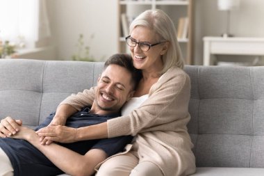 Neşeli kahkahalar atan son sınıf annesi, neşeli yakışıklı oğluna özenle sarılıyor, kanepede dinleniyor. Mutlu anne ve yetişkin çocuk evde buluşuyor, eğleniyor, aile eğlencesinin ve rahatlığın tadını çıkarıyor.