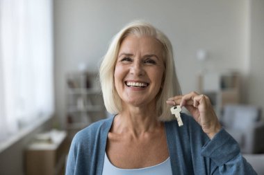 Yakın çekim portresi mutlu yaşlı kadın kameraya bakın, yeni dairenin anahtarlarını gösteriyor, kendi evini almak için heyecanlı, modern eve taşınıyor, ipoteğin son ödemesini kutluyor. Emlak