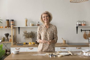 Mutlu olgun bir bayan mutfakta ev yapımı kurabiyeler pişiriyor, fırın malzemeleriyle bir parça çiğ hamur tutuyor, mutfak hobisinin tadını çıkarıyor, kameraya bakıyor, gülümsüyor. Baker portresi