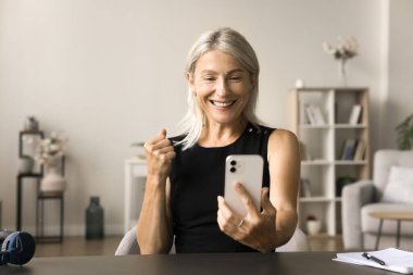 Neşeli, kıdemli akıllı telefon kullanıcısı cep telefonuyla konuşan, iletişimin tadını çıkaran, kazanan el yapan, gülümseyen, kutlama yapan, başarıyı kutlayan, başarı kazanan,