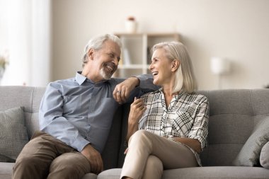 Mutlu, evli çift evdeki kanepede dinleniyor, konuşuyor, gülüyor, emekliliği tartışıyor, tatil planlarını tartışıyor, aile eğlencesinin tadını çıkarıyor, iyi bir ilişki, sevgi, yakın oturmak, gülüyor.