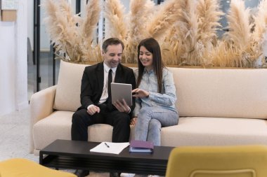 Ofis lobisinde tablet bilgisayar kullanan, projeyi tartışan, koltukta oturan, gülümseyen, konuşan, konuşan, ekrana bakan, internetten içeriği izleyen birkaç mutlu iş arkadaşı.