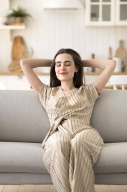 Mutlu, güzel, yetişkin bir kız kanepeye uzanıyor, gözleri kapalı, temiz hava soluyor, sırtına yaslanıyor, şekerleme yapıyor, rahatlıyor, dinleniyor, duraklıyor, başarıyor, meditasyon yapıyor.