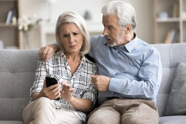 Endişeli yaşlı çift birlikte cep telefonu kullanıyor. Endişeli yetişkin eş şaşırmış yaşlı kocaya akıllı telefon ekranı gösteriyor, iletişim problemini tartışıyor, sorun yaşıyor.