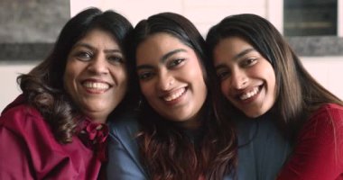 Mutlu, çekici, çok nesilli Hintli kadınların portresi. İki yetişkin kız ve orta yaşlı anne gülümsüyor, evde oturmuş kameraya bakıyor. Aile bağları, bağ ve birlik