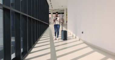 Ciddi genç Afrikalı bir kadın havaalanı terminalinde yürürken, gideceği yere varırken, elinde akıllı telefon, taksi çağırırken, mobil uygulama hizmetleri kullanarak transfer emri verirken. İş gezisi