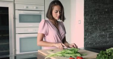 Modern mutfakta yeni yetme güzel bir kadın yemek pişiriyor, vejetaryen yemeği için taze sebze doğruyor, zayıflama için diyet yemeği hazırlıyor, sağlıklı yaşam tarzını koruyor, kilo verme tarifi hazırlıyor.