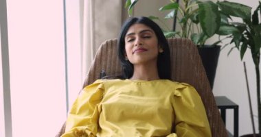 Güzel, barışçıl, güzel, gülümseyen bir Hintli kadın, evde tek başına dinleniyor rahat koltuğa yaslanıyor, gözlerini kapatıyor ve modern dairede temiz hava soluyor. Akıllı ev, eğlence, hayaller