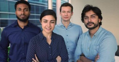 Motive olmuş ekip üyelerinin portresi, dört mutlu takım arkadaşı ofiste profesyonel başarılara hazır. Çok uluslu çalışanlar kameraya bakıp gülümsüyor, birlikte duruyor, birlik gösteriyor.