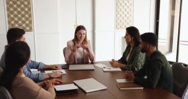 Genç çok ırklı iş adamlarından oluşan bir grup toplantı odasında toplandı, kadın takım liderinin konuşmasını dinlediler, şirket hedefleri hakkında konuştular, proje detaylarını anlattılar, toplantıda rapor verdiler.