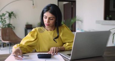 Çekici, genç Hintli bir kadın masa başında oturur, faturaları internetten öder, dizüstü bilgisayar kullanır, aylık bütçeyi sayar, ödeme yapar, finansal belgeleri kontrol eder. Ciddi bir kadın hesap makinesi ile gelir hesaplar. E-bank