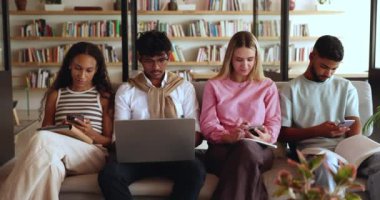 Z Geni öğrencileri kütüphanede çeşitli modern kablosuz cihazlar kullanıyorlar, çalışmaktan, sohbet etmekten, mobil online uygulamalar aracılığıyla programı kontrol etmekten kaçıyorlar, birbirlerini görmezden geliyorlar, internet kullanımına gömülüyorlar.